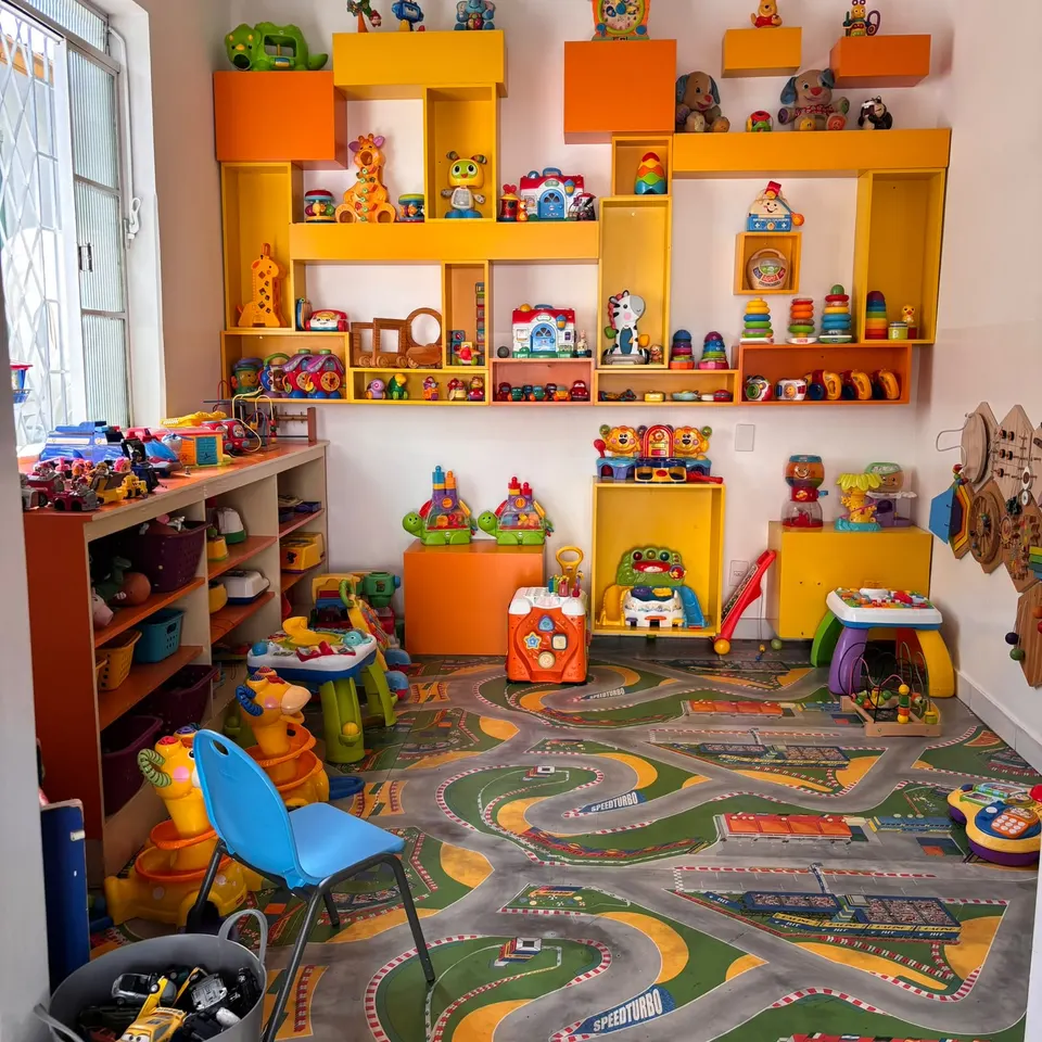 A sala dos brinquedos, com prateleiras amarelas e laranja e um tapete em forma de pista de carrinhos
